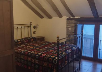 Casa Batán - dormitorio principal con vigas de madera y balcón en Larrés